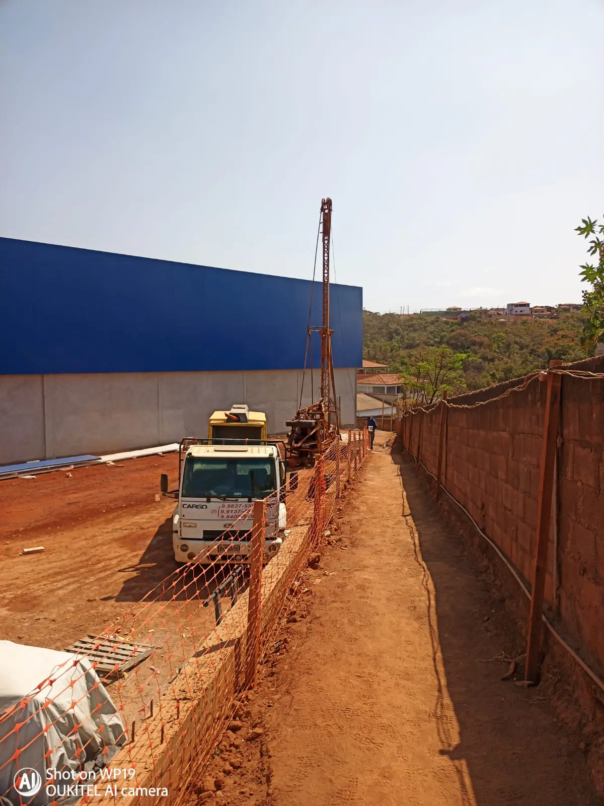 Equipamento de perfuração em operação ao lado de galpão em construção.